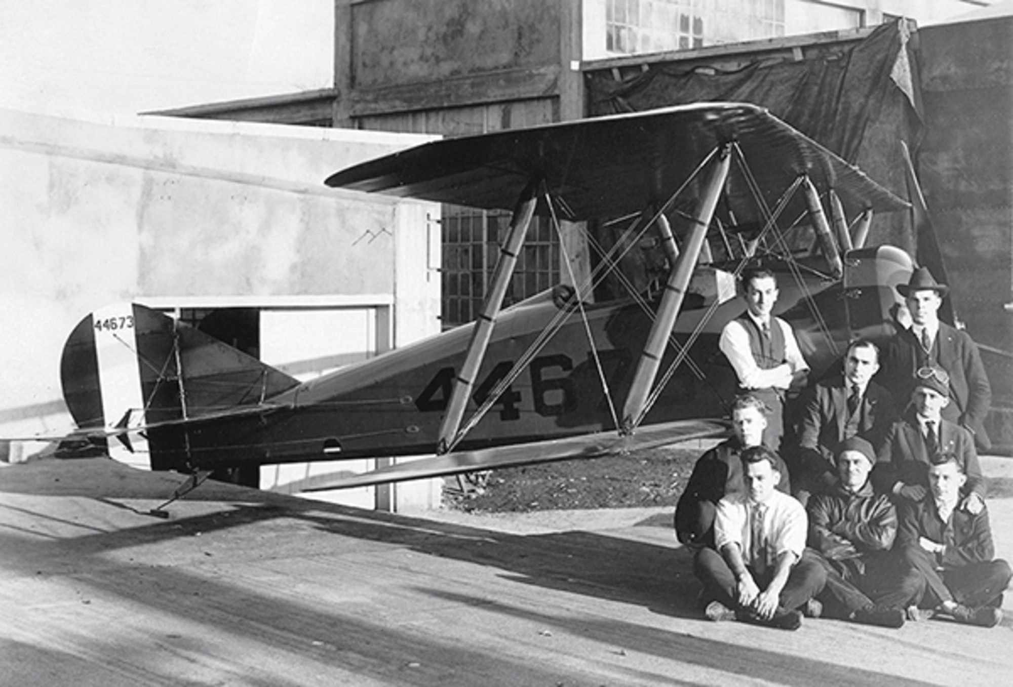 Black and white image of a group of people sitting in front of a Tommy Morse plane