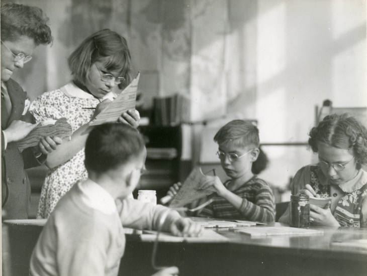 Black and white photograph of male and female students working on wood cutouts. Image taken circa 1938. Image from Ithaca's Open Air School Sight Saving Class. School began in 1917 to focus on students who were at high risk for tuberculosis. Sight Saving Class was begun to focus on students with visual impairments. 