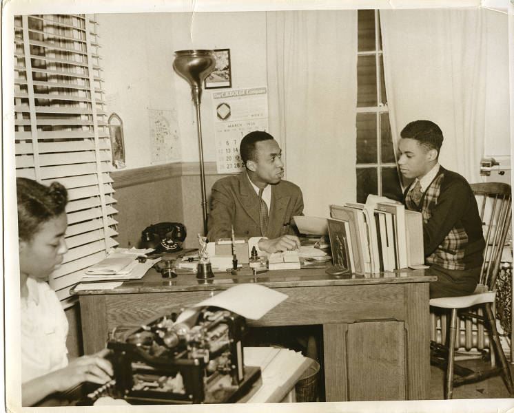 Image of Mr. Gibbs sitting in an office with a young man and a woman typing on a typewriter.