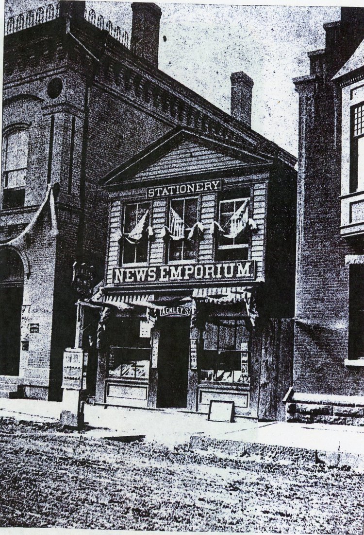 An image of a building with a sign that says "News Emporium". Caption reads "Ackley's News Emporium - After 1881".