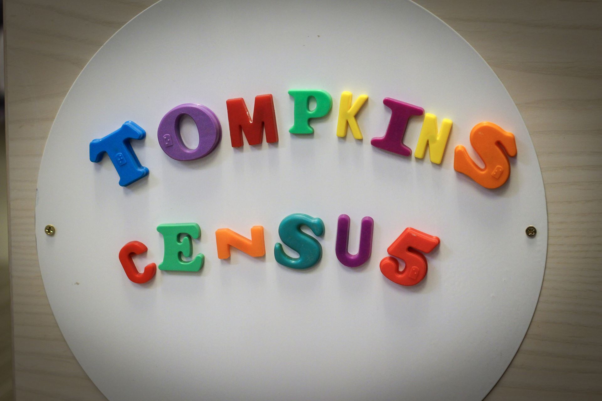 A rectangular image of colorful letter magnets that read "Tompkins Census". The 'n' in census uses a horizonal z and the 's' uses a 5.