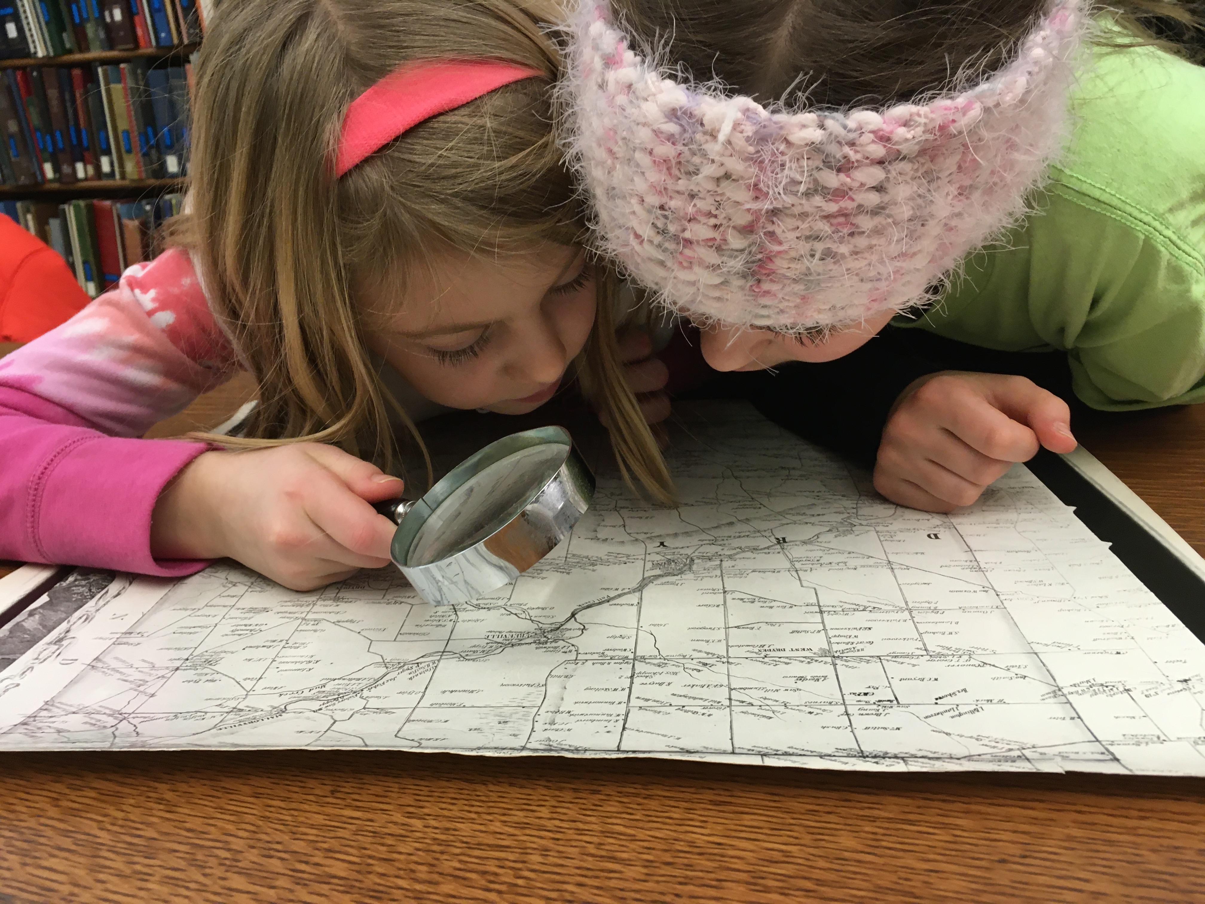 Image of two kids looking at a map with a magnifying glass